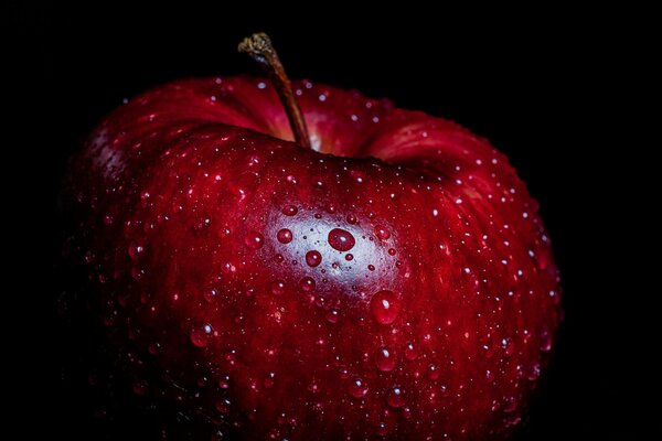 Manzana roja brillante en gotas de agua sobre un fondo negro