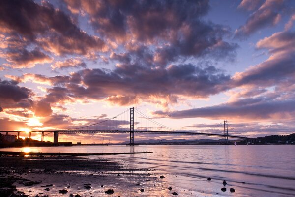 The bridge on the background of sunset. A calm river. The clouds