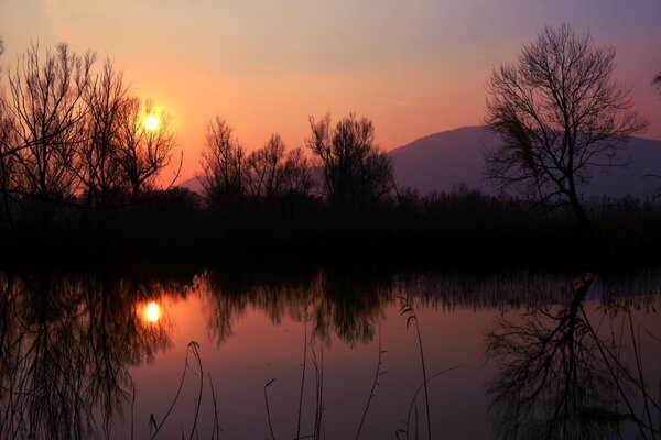 Il sole arancione al tramonto si riflette nel lago