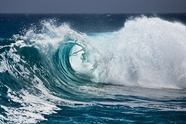 Alta onda di schiuma con spruzzi tra l oceano e il cielo grigio all orizzonte