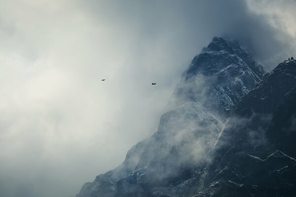 Die Berge des Himalaya im Schnee mit fliegenden Vögeln in den Wolken