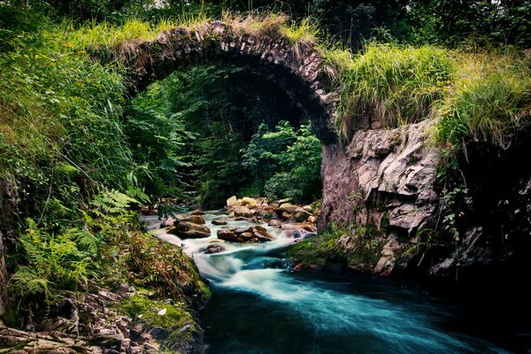 Stone semicircular bridge over a stormy rocky river