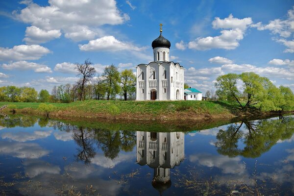 A white church with a blue dome on the shore of a blue lake