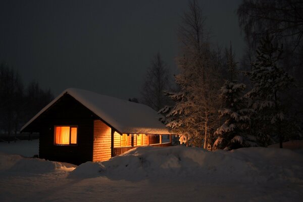 Warmes Licht im Winter, das am Abend aus dem Haus auf den Schnee locht