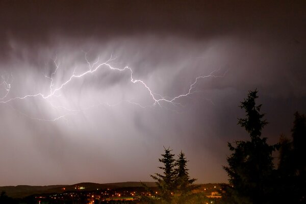 Über der Nachtstadt durchschneidet ein Blitz einen dicken Schleier von braunen Wolken