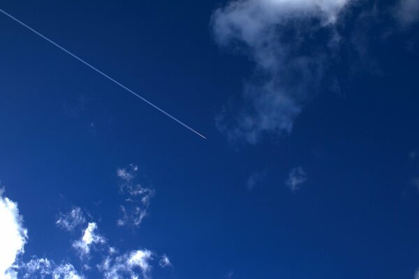 Die Spur des Flugzeugs am blauen Himmel unter den Wolken