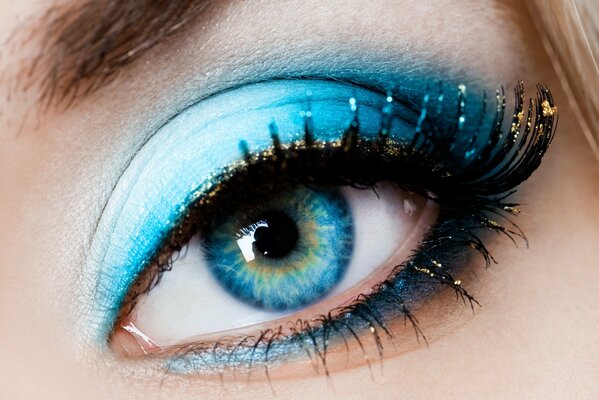 The girl s eye is a close-up of blue color, with blue shadows and golden eyelashes