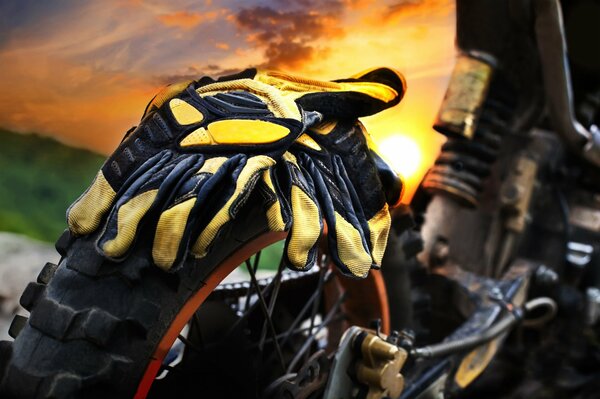 Gants de moto jaune sur une moto sur fond de soleil couchant