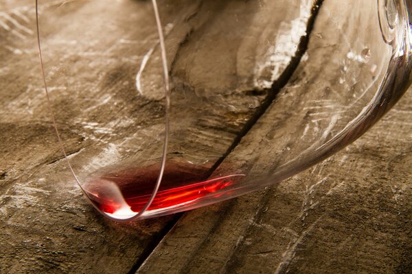 A drop of red wine in a glass was dripping onto a wooden table