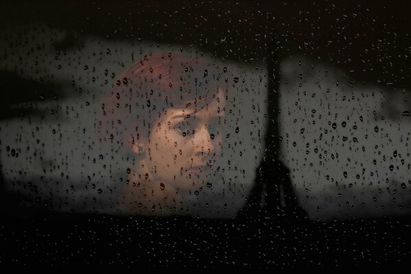 Silhouette eines Mädchens durch ein Fenster mit Tropfen