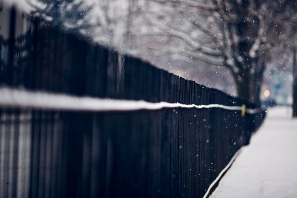 Długie czarne ogrodzenie wzdłuż zaśnieżonej drogi