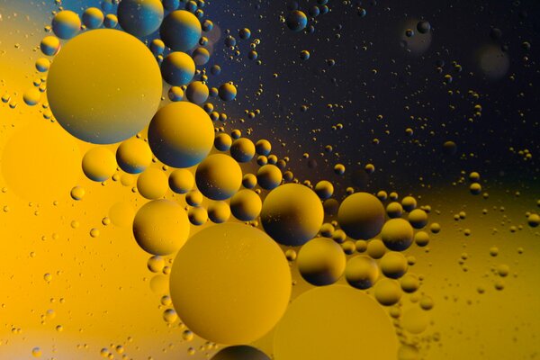 En el agua, gotas de aceite de diferentes tamaños sobre un fondo amarillo-azul