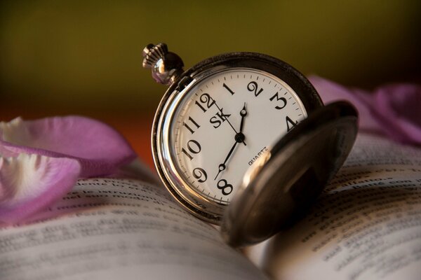 The clock on the book. Rose petals on the book