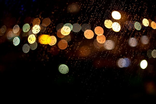 Por la noche, cuando estás sentado en el coche está lloviendo goteando de vidrio se ve multicolor