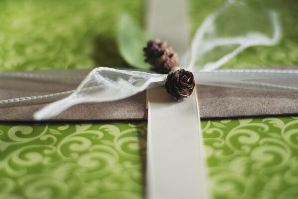 Macro gift box of green color with white monograms and a gray satin ribbon decorated with cones and a white transparent bow
