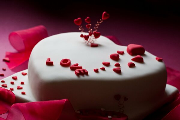 A heart-shaped cake covered with white mastic with the inscription Love