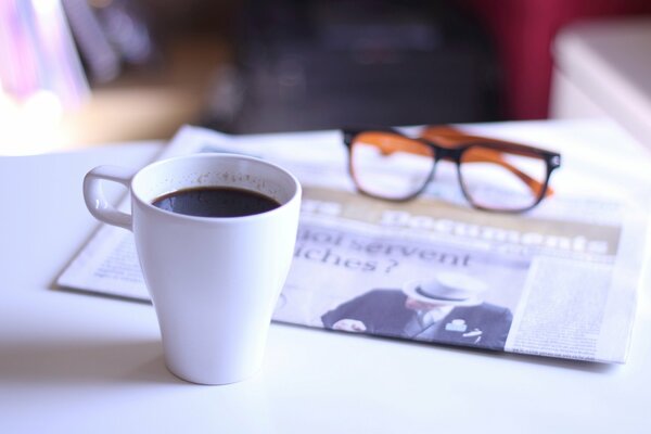 A cup of coffee glasses and a newspaper on the table