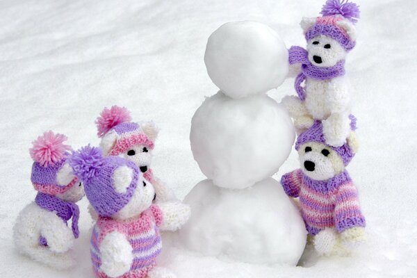 Gestrickte Bären auf einem Schneemann in lila Mützen