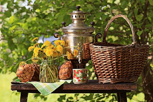 Still life of a table with a samovar, basket, greenery on the background of nature