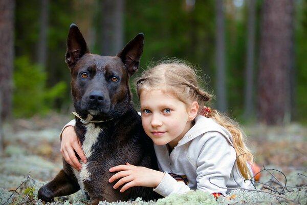 A girl in an embrace with a dog in the forest