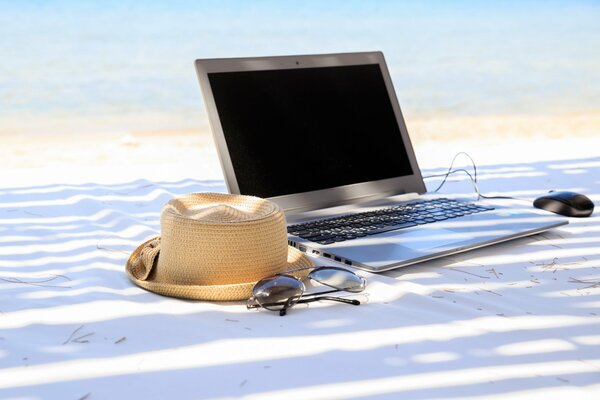 Ein Laptop und ein Hut liegen auf weißem Sand