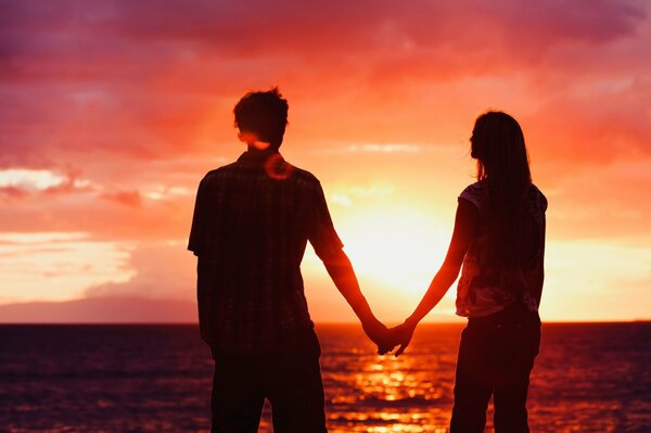 A guy and a girl holding hands against the sunset