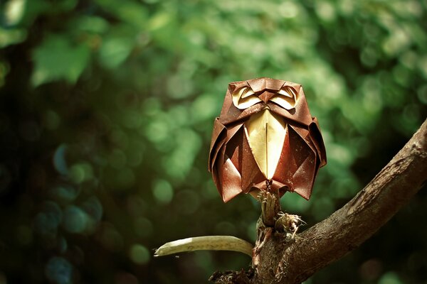 An origami-style owl sitting on a branch in a green forest