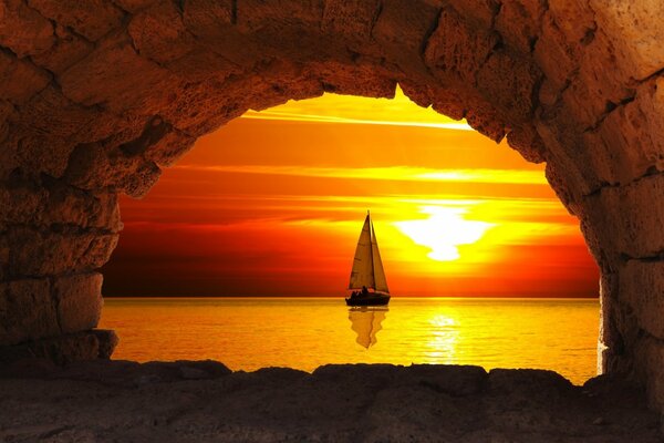 View of a boat with a white sail on the background of the evening sky through the arch