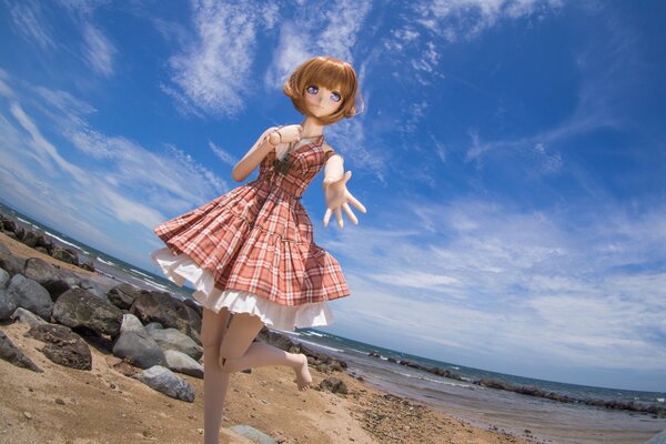 Muñeca de juguete en vestido en la playa junto al mar