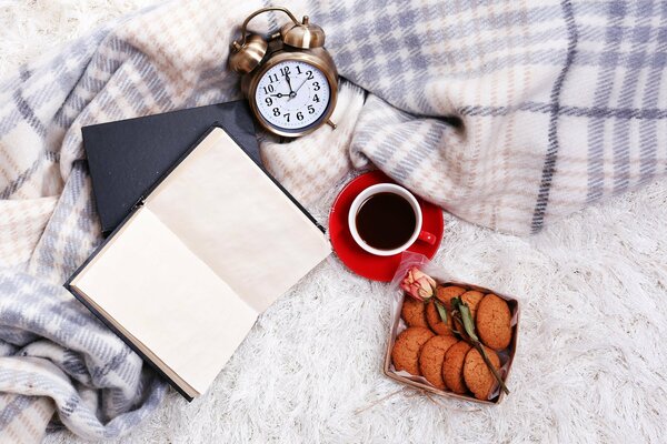 Der Wecker liegt auf einem Plaid neben einem Buch und einem Kaffee