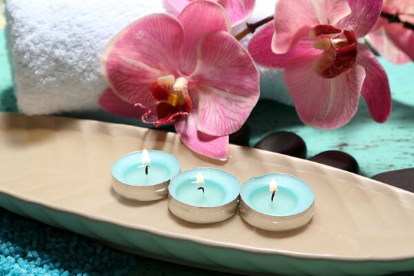 Три горящие свечи. На заднем фоне белое полотенце и орхидеи
