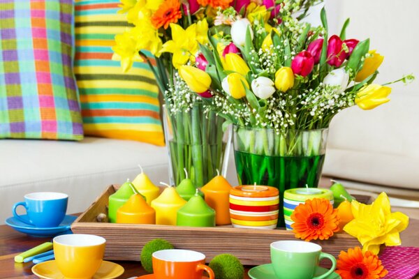 Bunte Anordnung von bunten Tassen und Kerzen auf einem Tisch mit Tulpen und Servietten