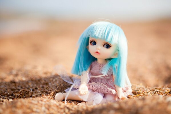 Sitting doll on the sand with blue hair