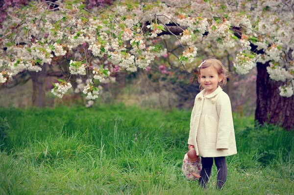 Девочка с куклой на фоне цветущего дерева