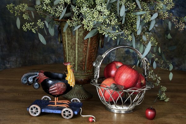 Still life with the image of red apples in a basket, a cockerel and a vase