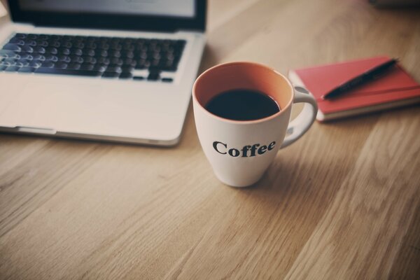 Чашка с кофе, белый ноутбук и красная записная книжка на деревянном столе