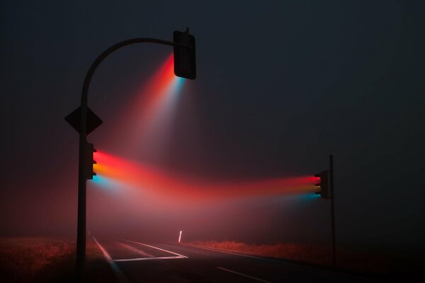 Traffic lights with their colored rays disperse the fog from the night road