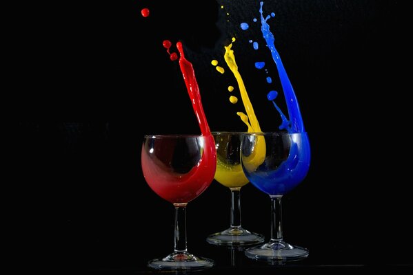 Three glasses with a multi-colored liquid pouring out on a black background
