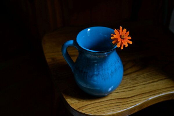 Una brocca blu con un fiore arancione sta su una sedia di legno