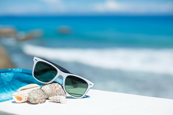 Okulary przeciwsłoneczne, muszle, niebieskie pareo na białej ławce. Morze
