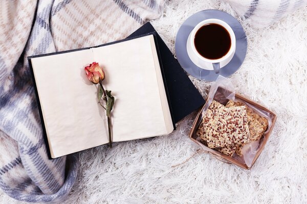 Imagen de un Bloc de notas y una rosa en el fondo de una manta cálida y una taza de café caliente
