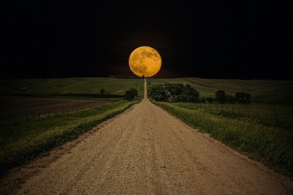 Długa droga w polu na horyzoncie żółknie okrągły księżyc