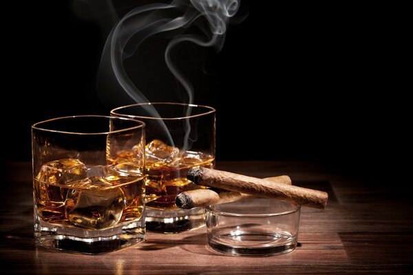 Un vaso de whisky con hielo y cigarros