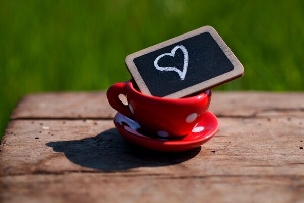 Rote Tasse in weiße Erbsen auf einer Untertasse mit einer Tafel, auf einer Tafel ein Herz mit Kreide