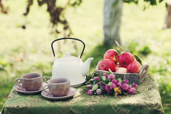 Sommerkomposition im Garten mit Teekanne, Tassen, Äpfeln und Blumen