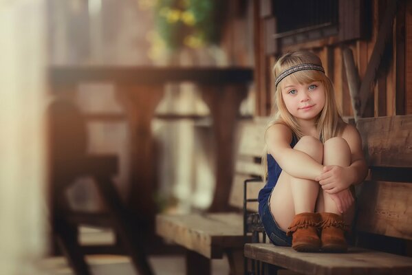 A little girl with blonde hair is sitting on a wooden bench