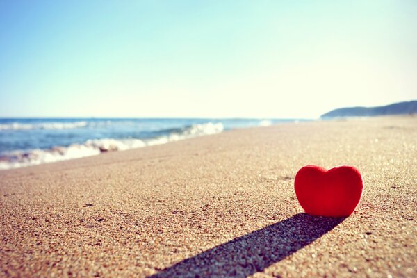 Cuore rosso sepolto nella sabbia sulla spiaggia