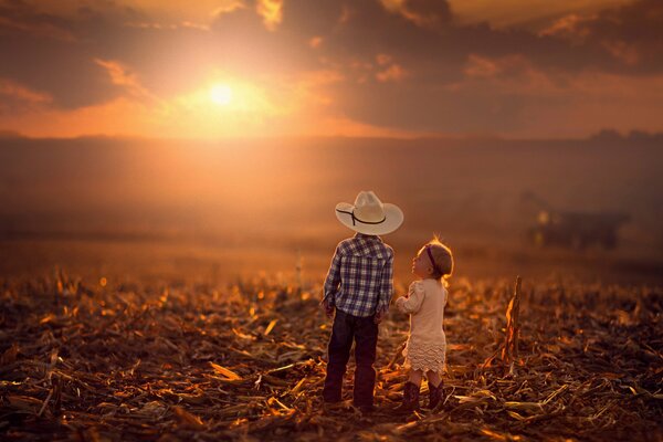 Un niño y una niña en el campo en el fondo de una puesta de sol de otoño