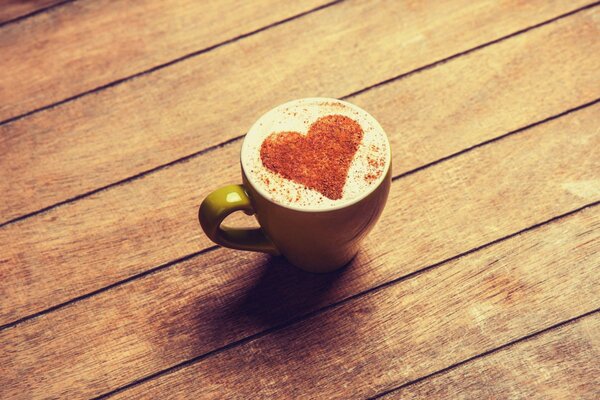 A green cup with coffee and a drawing in the form of a heart made of cocoa