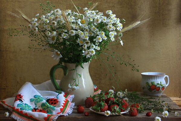 Kamillenvase auf einem Stod zusammen mit einer Tasse und einem Teller Erdbeeren